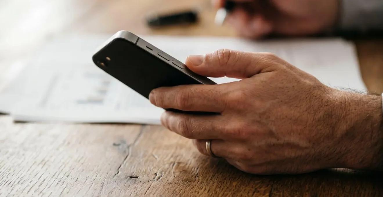 Main tenant un téléphone dans un environnement de travail épuré avec documentation floue en arrière-plan
